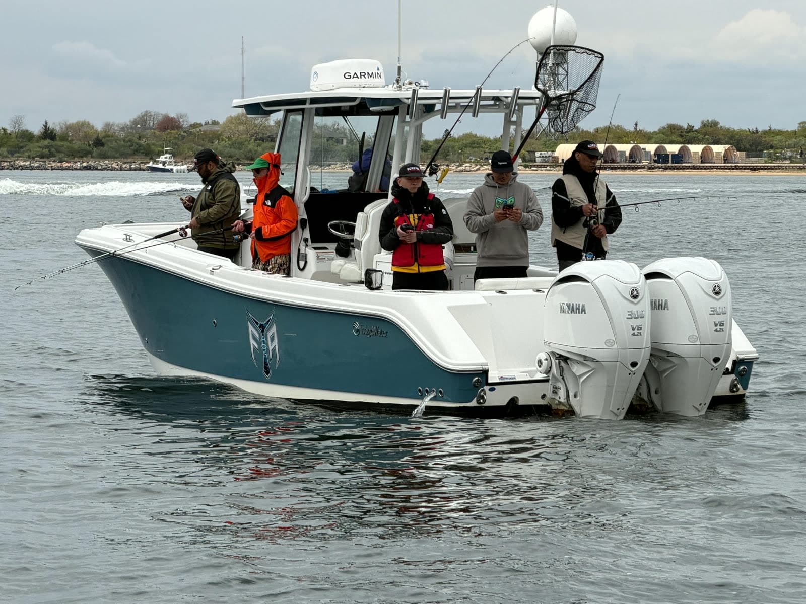 The Fishing The Atlantic boat with a full crew fishing the rail, twin outboards down and the shoreline behind.
