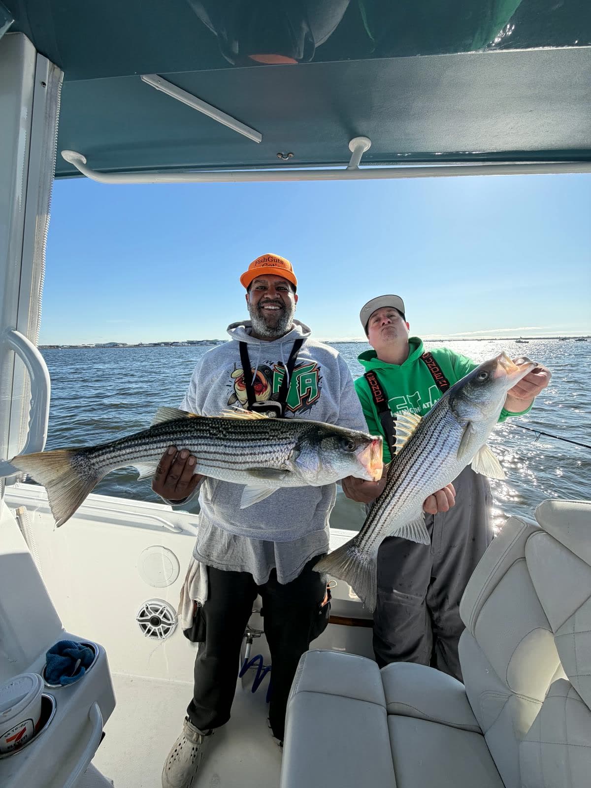 Two anglers under the hardtop holding three striped bass between them on a bright day.