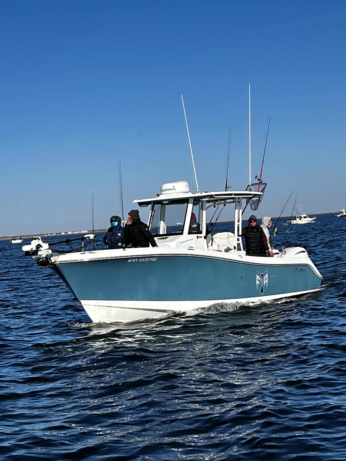 The Fishing The Atlantic boat underway — teal hull, hardtop with radar, rods in the holders and anglers aboard.